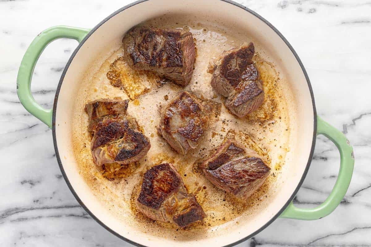 Large pan filled with seared beef chuck roast.
