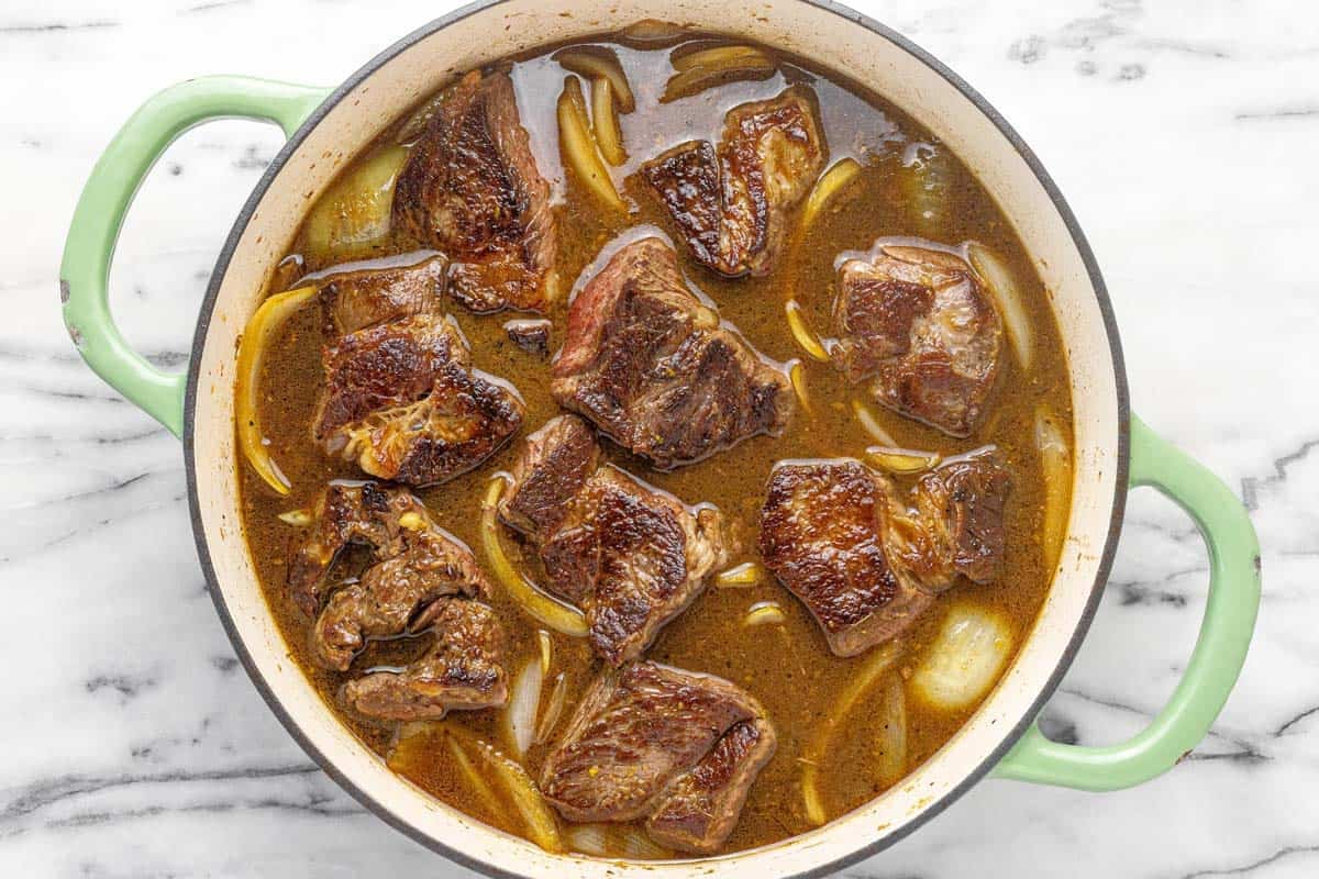 Seared beef chuck roast in a pan of veggies and braising liquid.