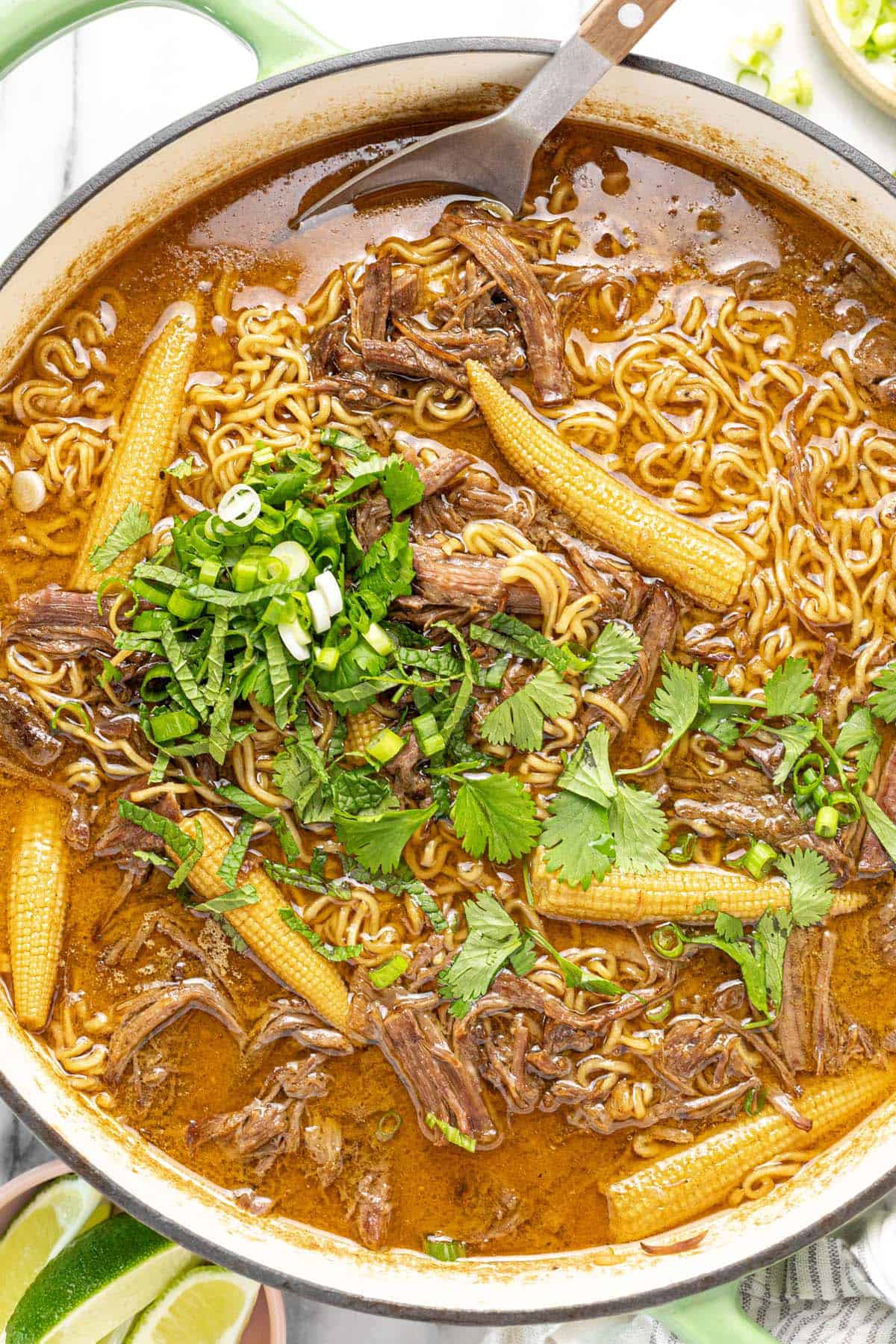 Large pot filled with shredded beef ramen garnished with cilantro and green onion.