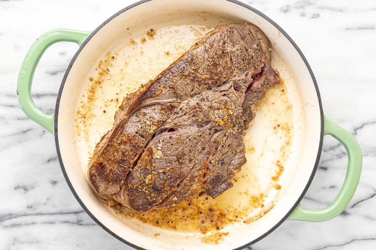 Seared chuck roast in a large pan.