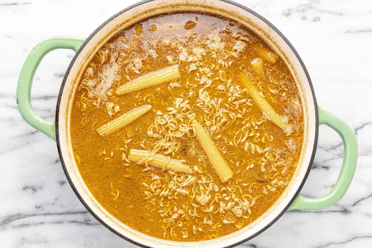 Ramen noodles and corn cooked in creamy coconut broth in a large pan.