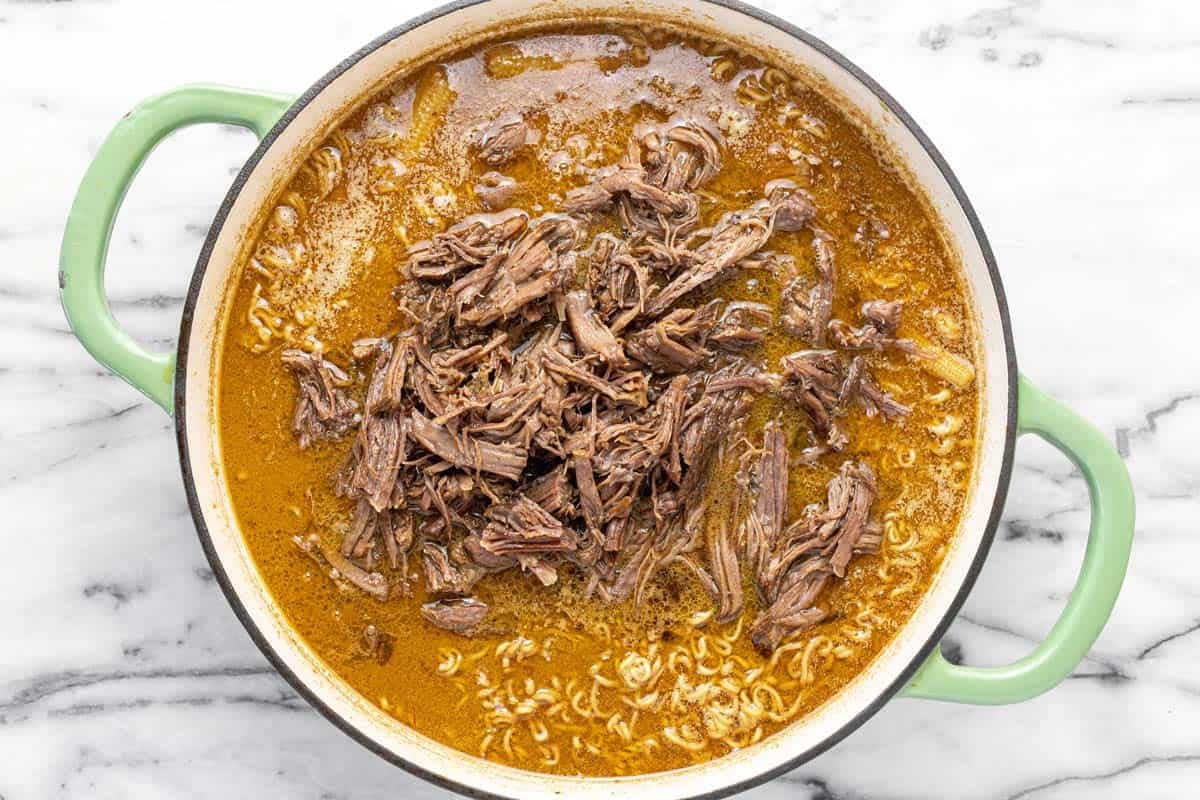 Shredded beef in a large pot of ramen soup.