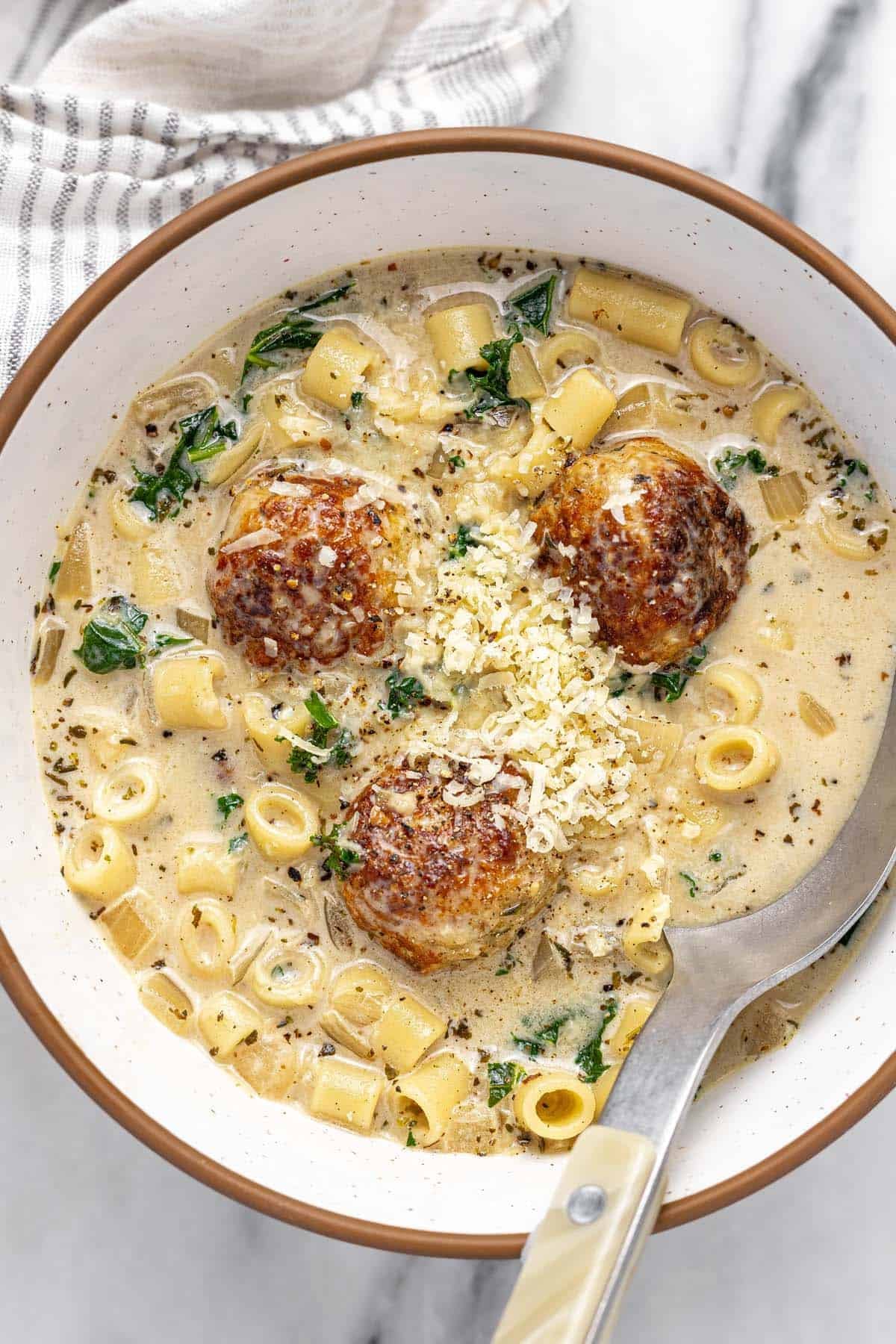 Bowl of chicken meatball noodle soup topped with Parmesan.