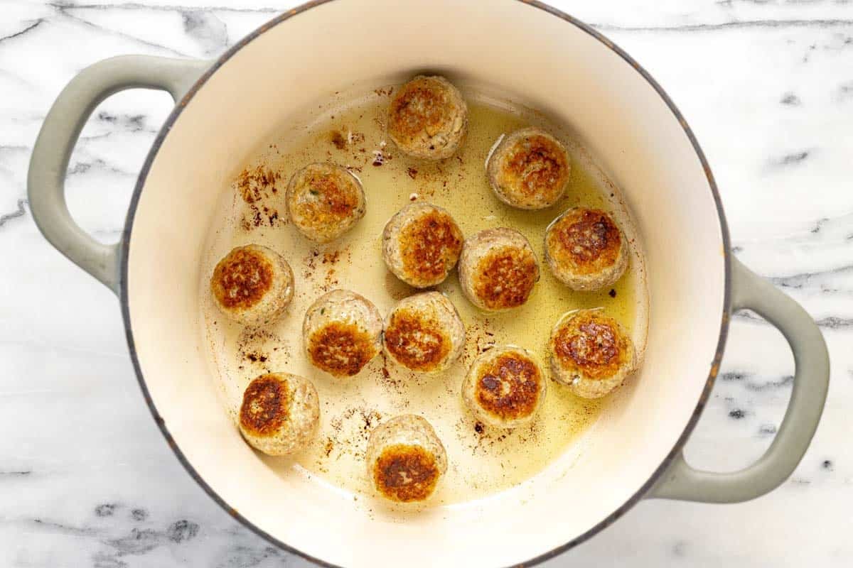 Seared chicken meatballs in a large pot with olive oil.