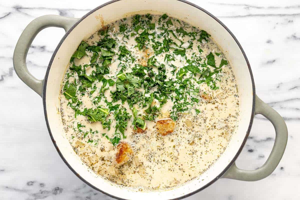 Chicken meatballs and kale in a large pot of creamy noodle soup.