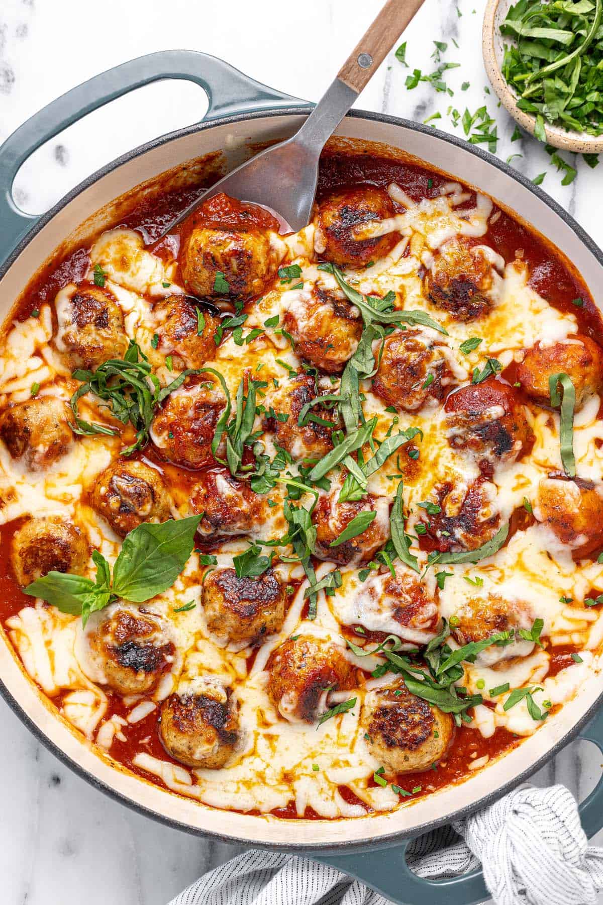 Large pan filled with chicken Parmesan meatballs garnished with basil and parsley.