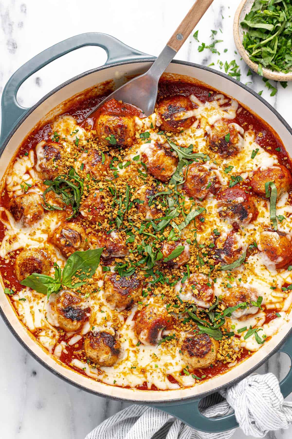 Large pan filled with chicken Parmesan meatballs garnished with breadcrumbs and basil.