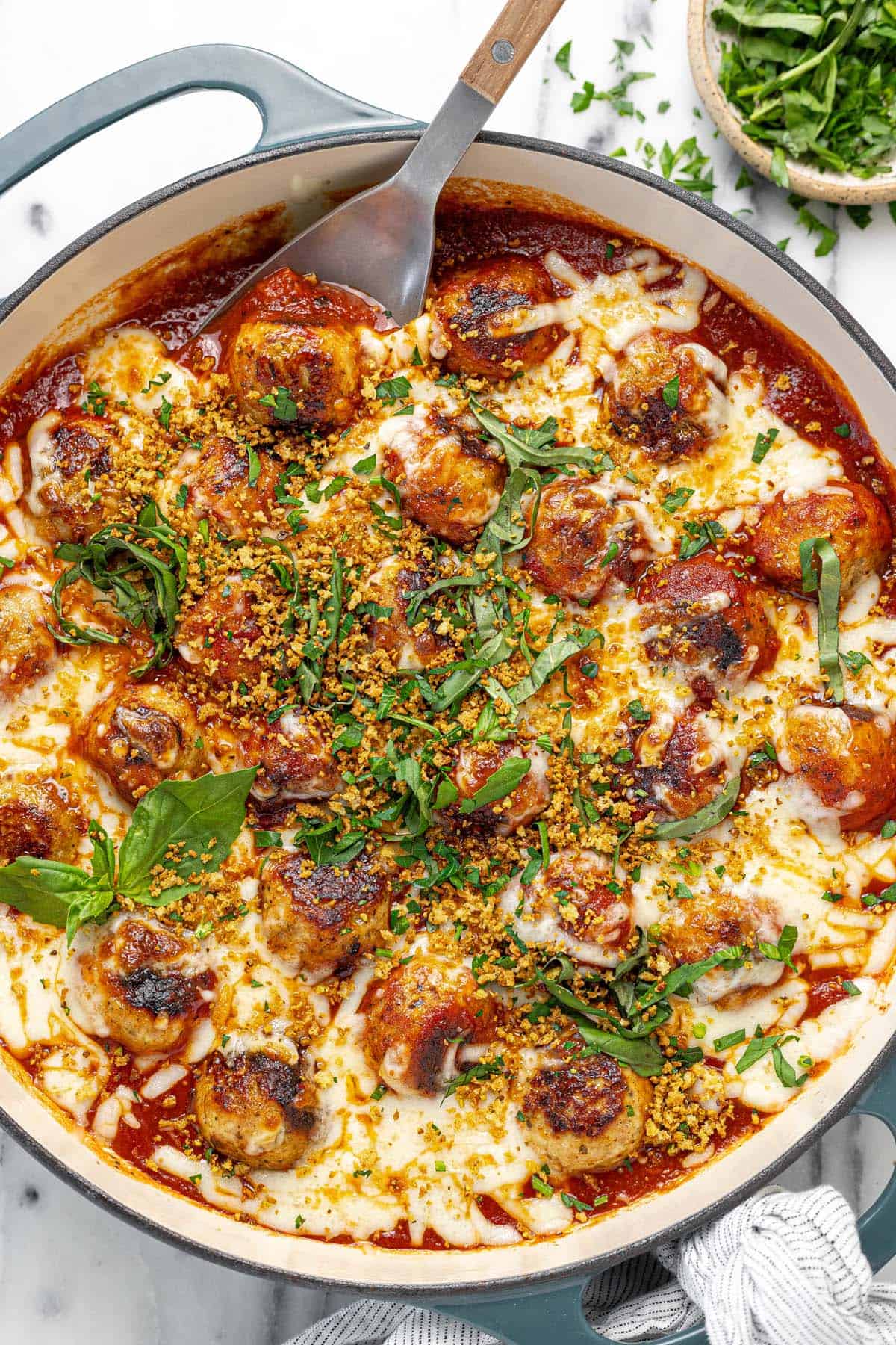 Large pan filled with chicken Parmesan meatballs garnished with breadcrumbs and basil.