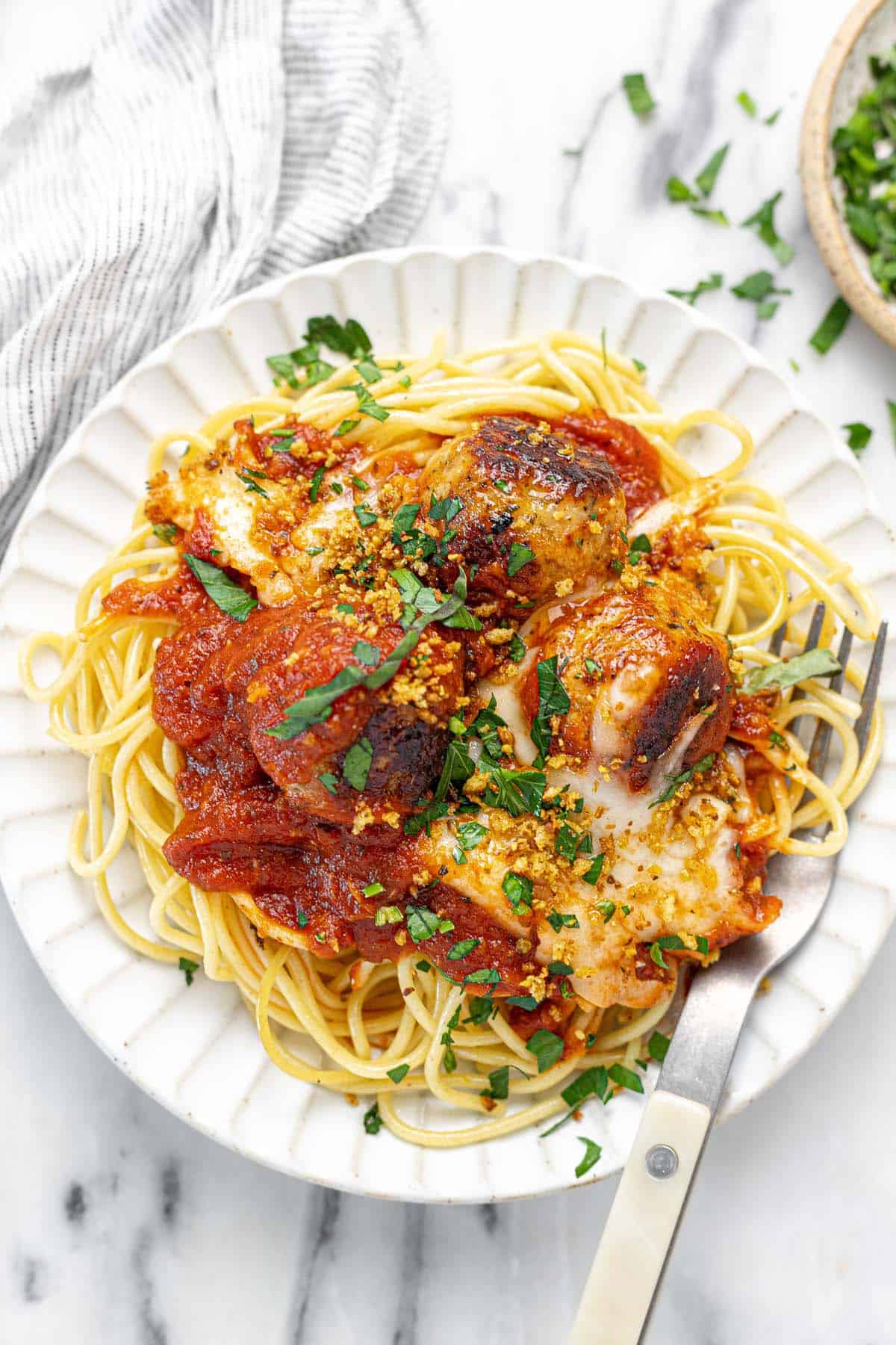 Plate of spaghetti and chicken Parmesan meatballs garnished with breadcrumbs and parsley.