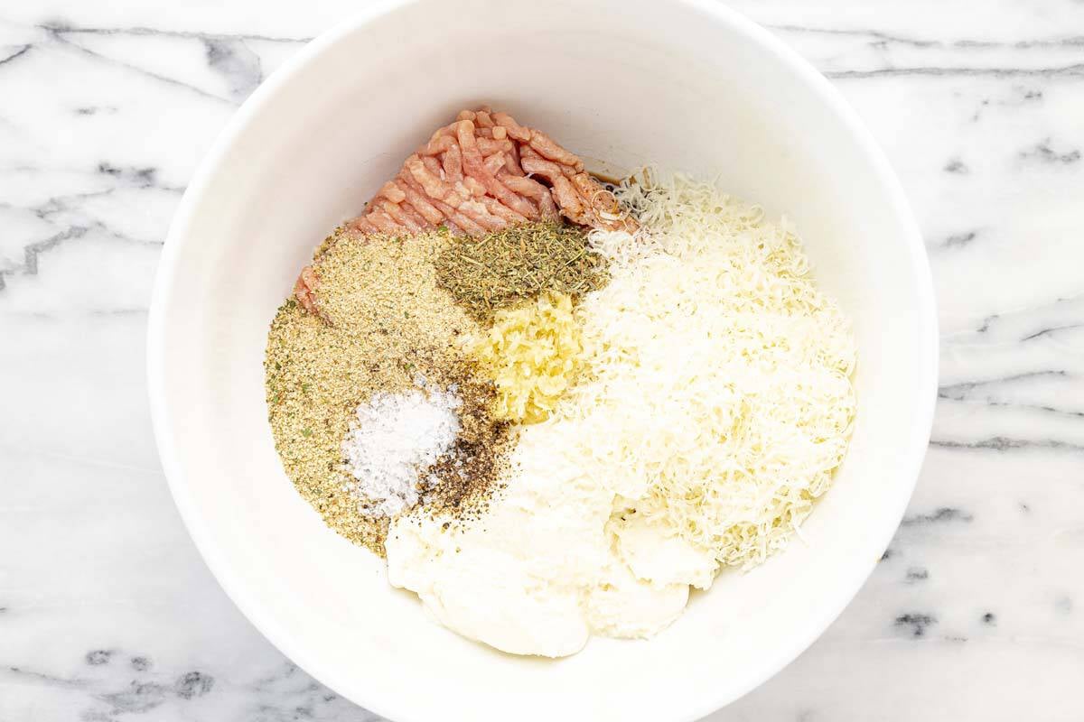 Large bowl filled with ingredients to make chicken meatballs.