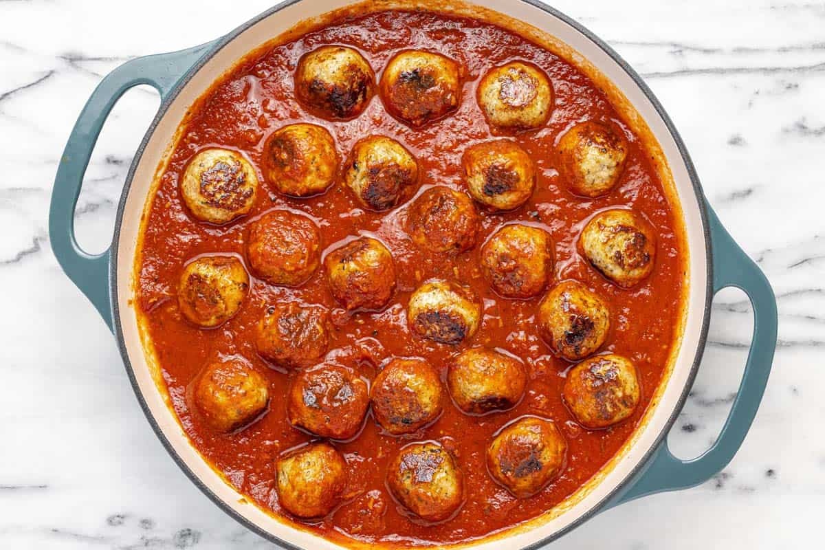 Chicken meatballs added to a pan of red sauce.