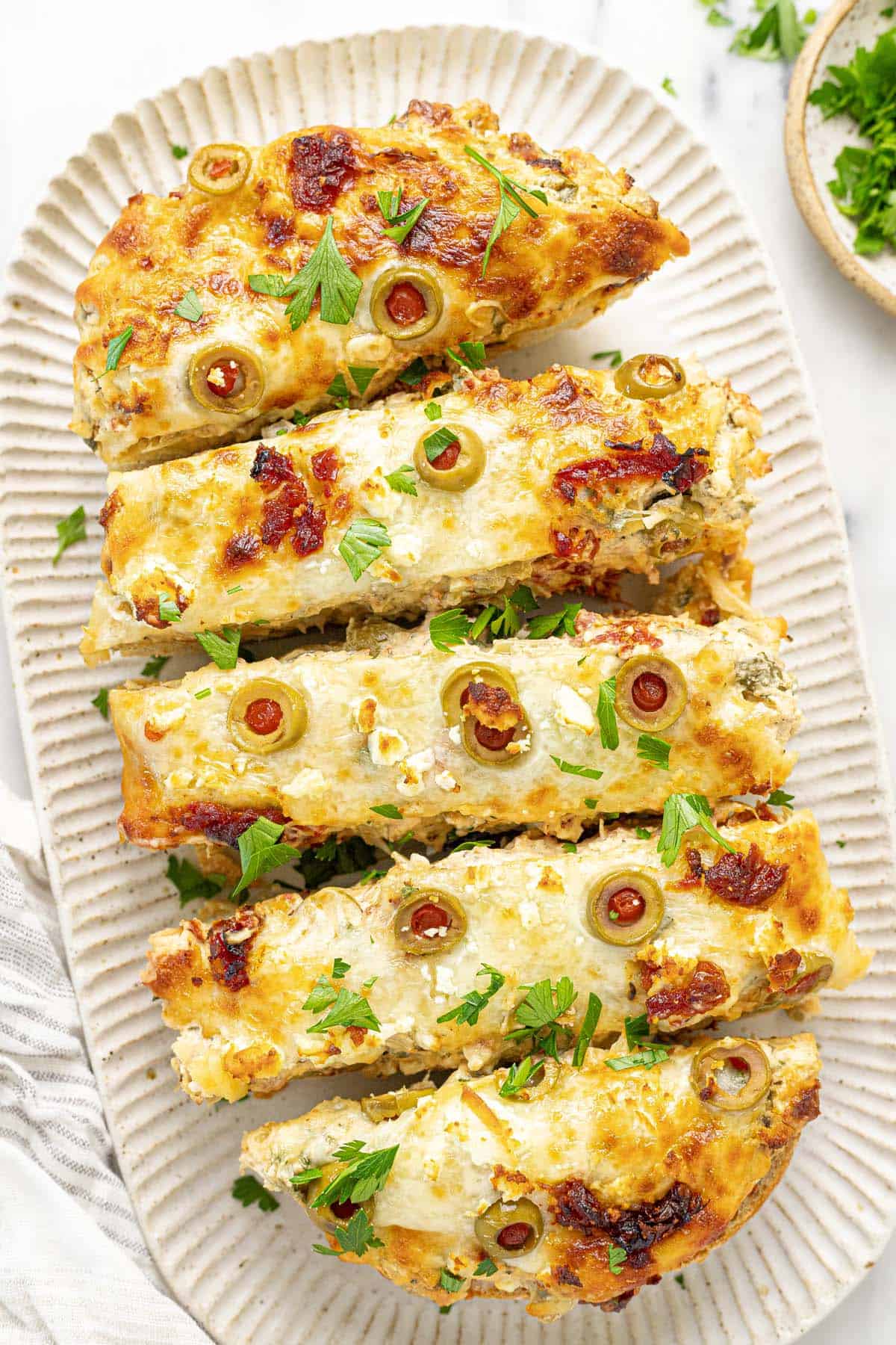 Serving platter with sliced Greek garlic cheese bread garnished with parsley.