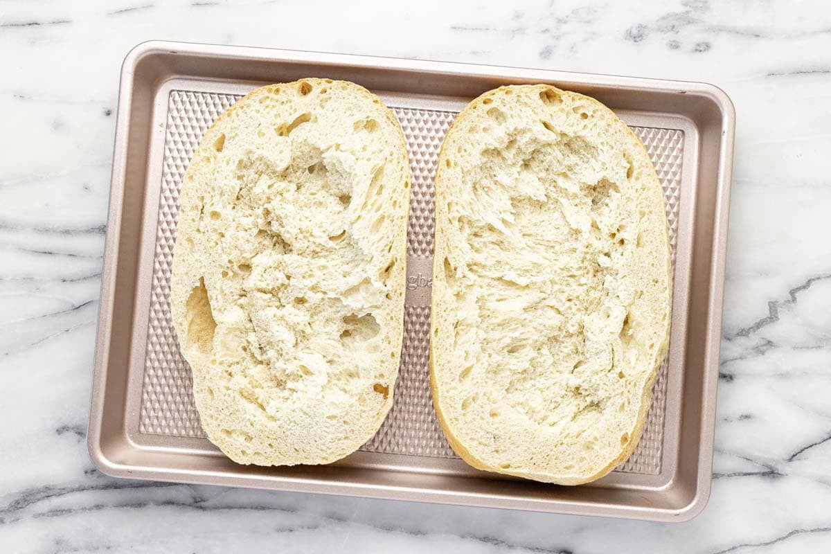 Loaf of Italian bread sliced in half on a baking sheet.