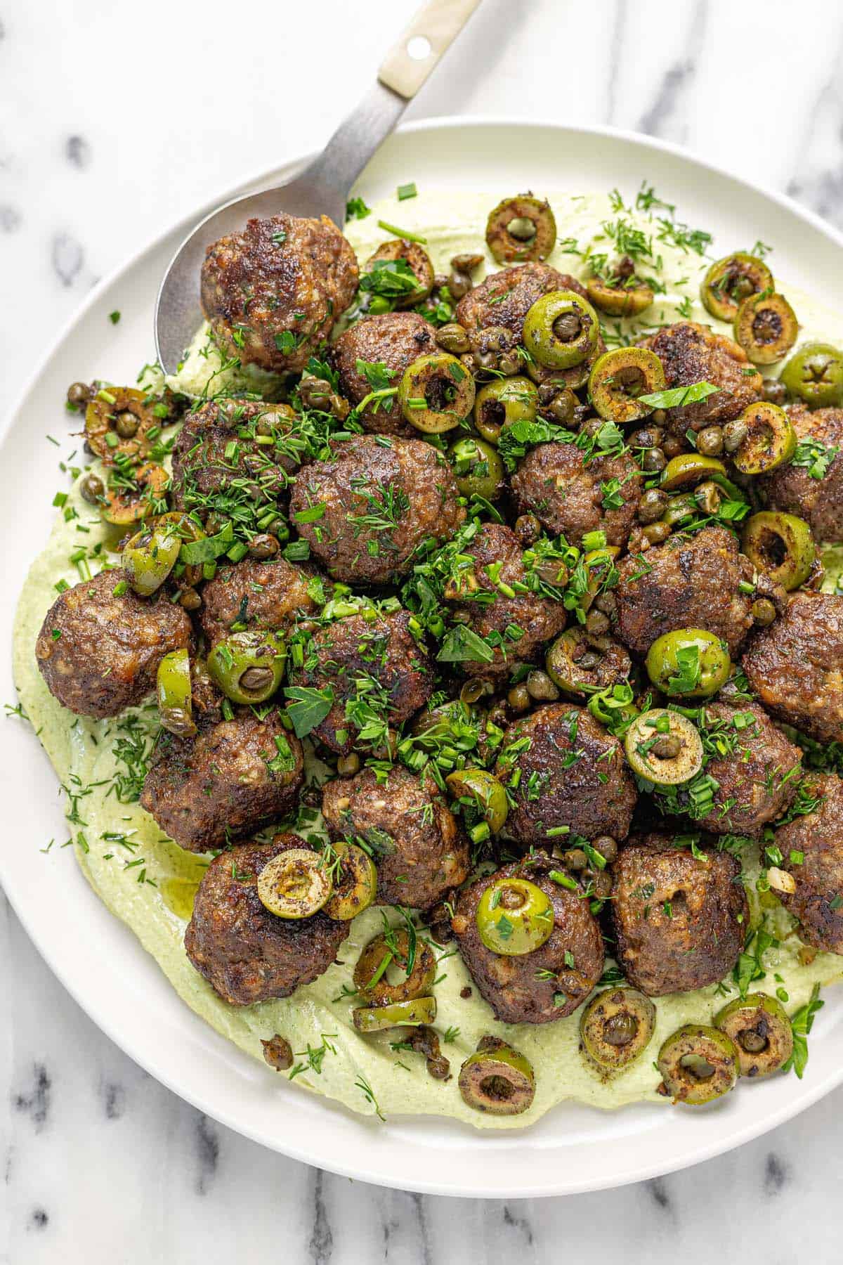 Large plate filled with whipped feta, meatballs, and olives.