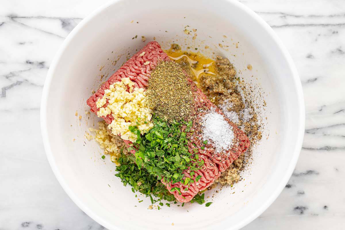 Large bowl filled with ingredients to make herby meatballs.