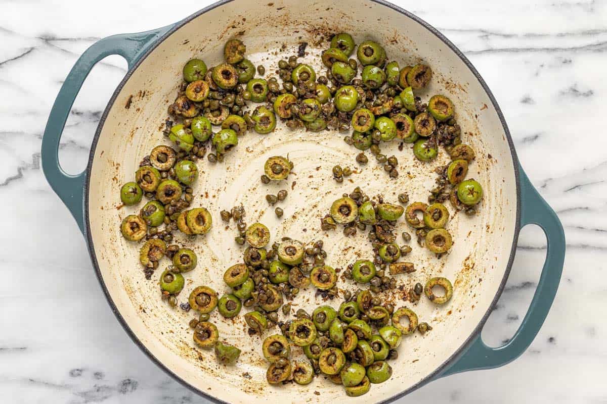Sauteed olives and capers in a large pan.