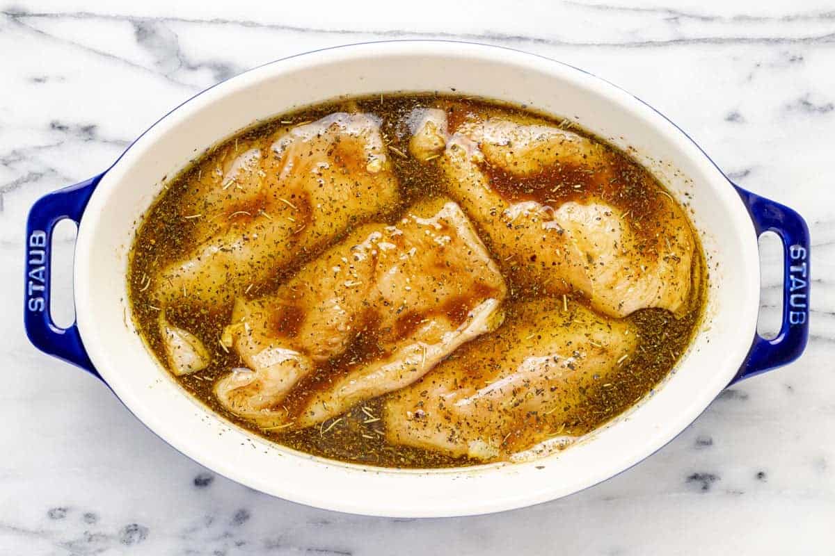 Chicken breasts marinating in a shallow dish of marinade.
