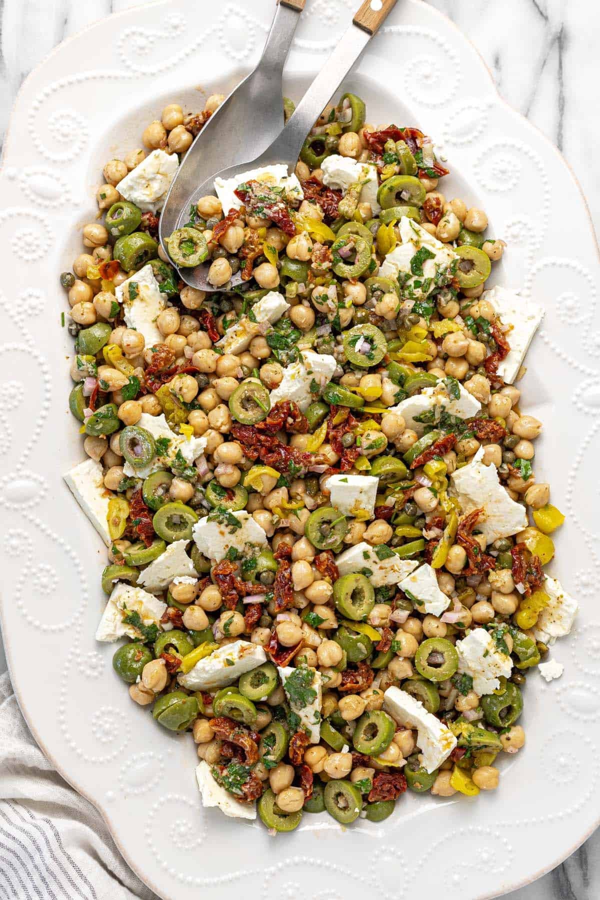 Serving platter filled with marinated chickpea salad with sliced feta.