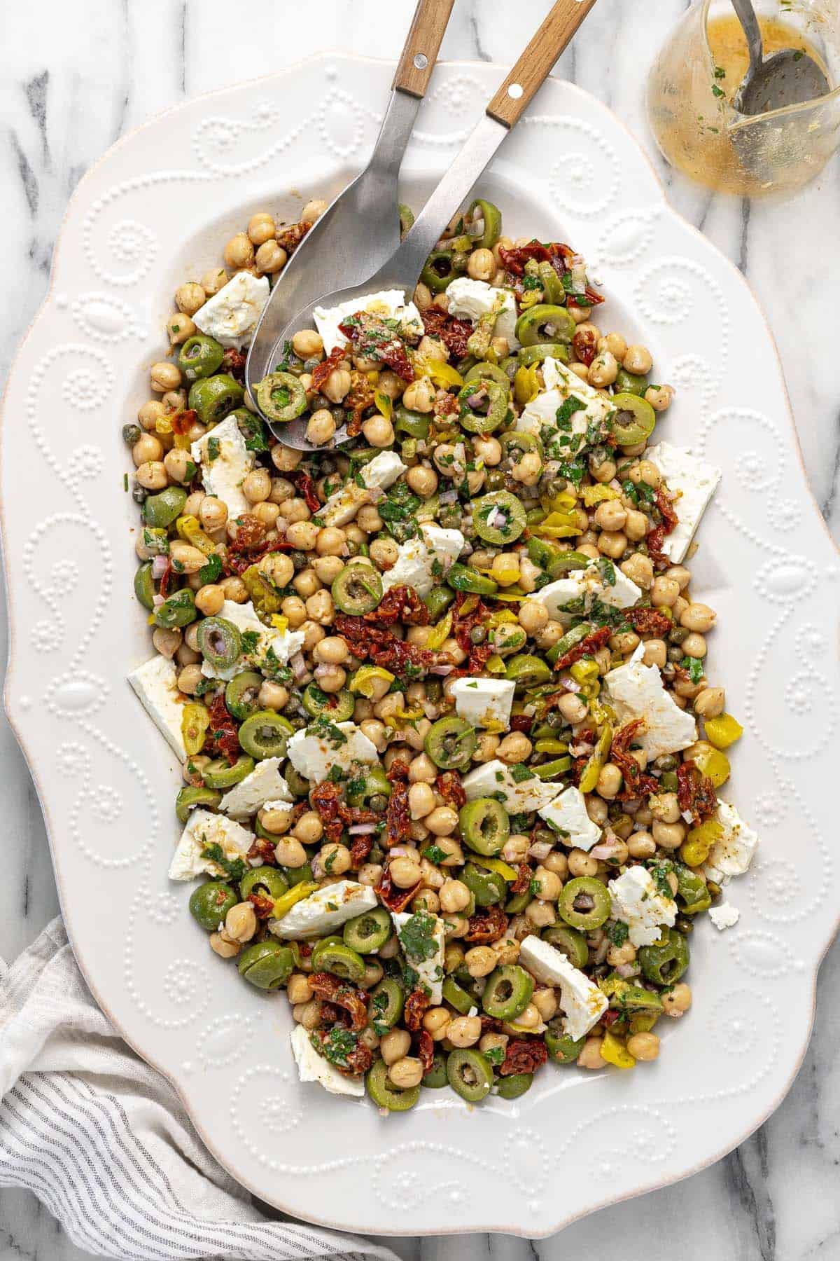 Serving platter filled with marinated chickpea salad with sliced feta.