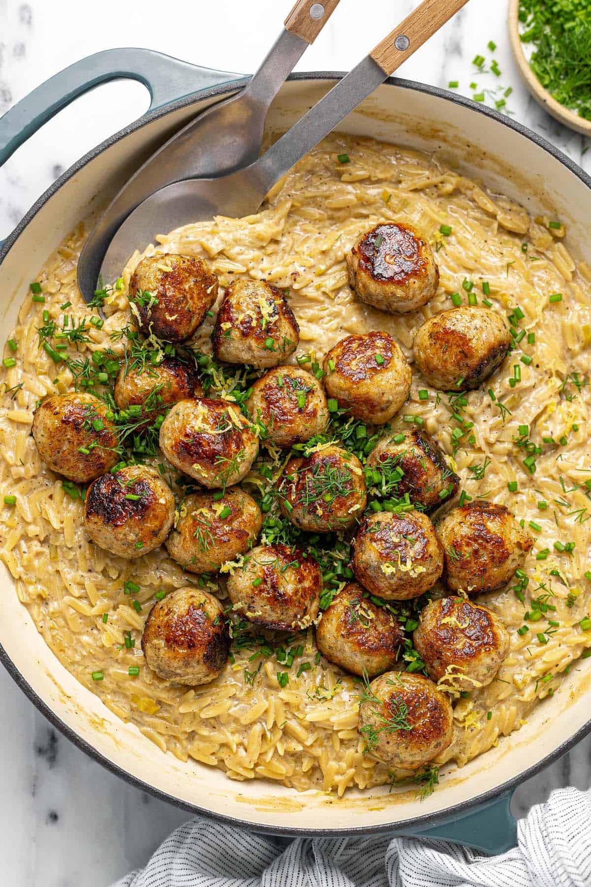 Large pan filled with chicken meatballs and cheesy orzo pasta with herbs.