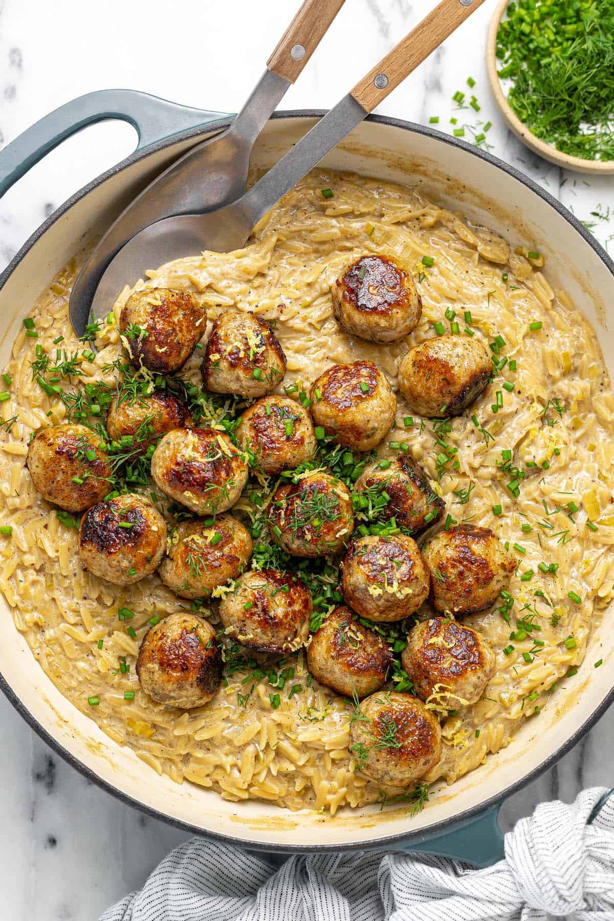 Large pan filled with chicken meatballs and cheesy orzo pasta with herbs.