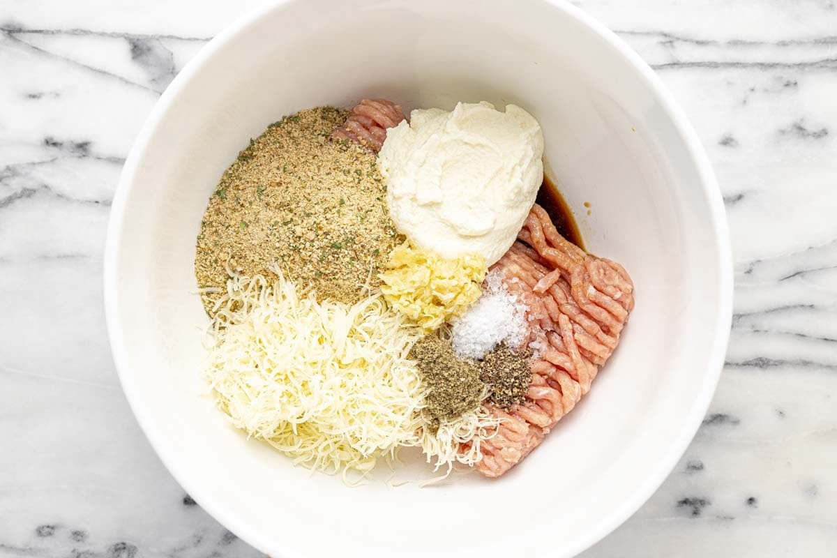 Large bowl filled with ingredients to make chicken meatballs.