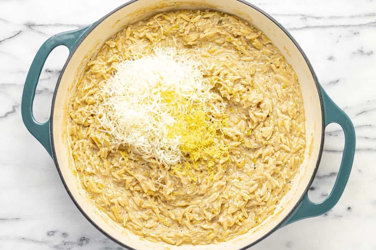 Creamy orzo in a large pan with Parmesan cheese and lemon zest.
