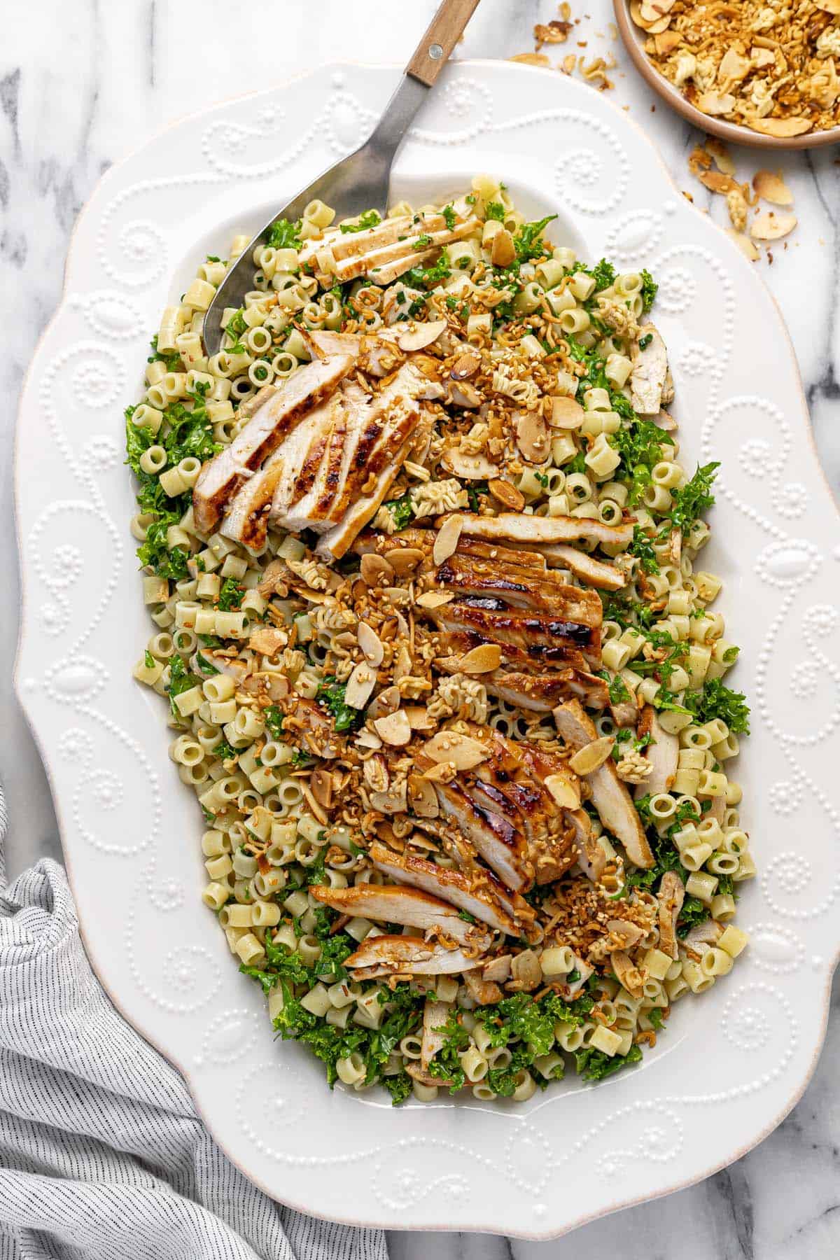 Large serving platter filled with sesame chicken pasta salad topped with crunchy ramen.