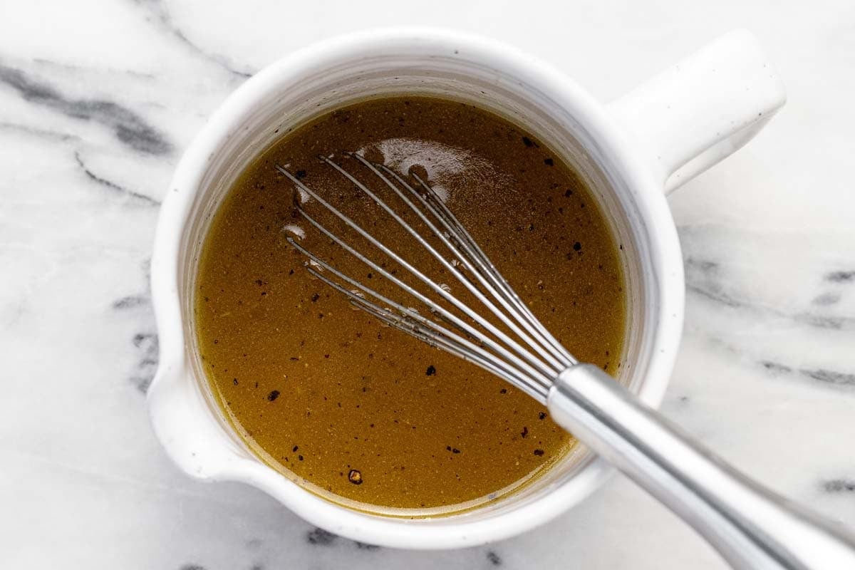 Large measuring cup filled with sesame dressing with a whisk in it.