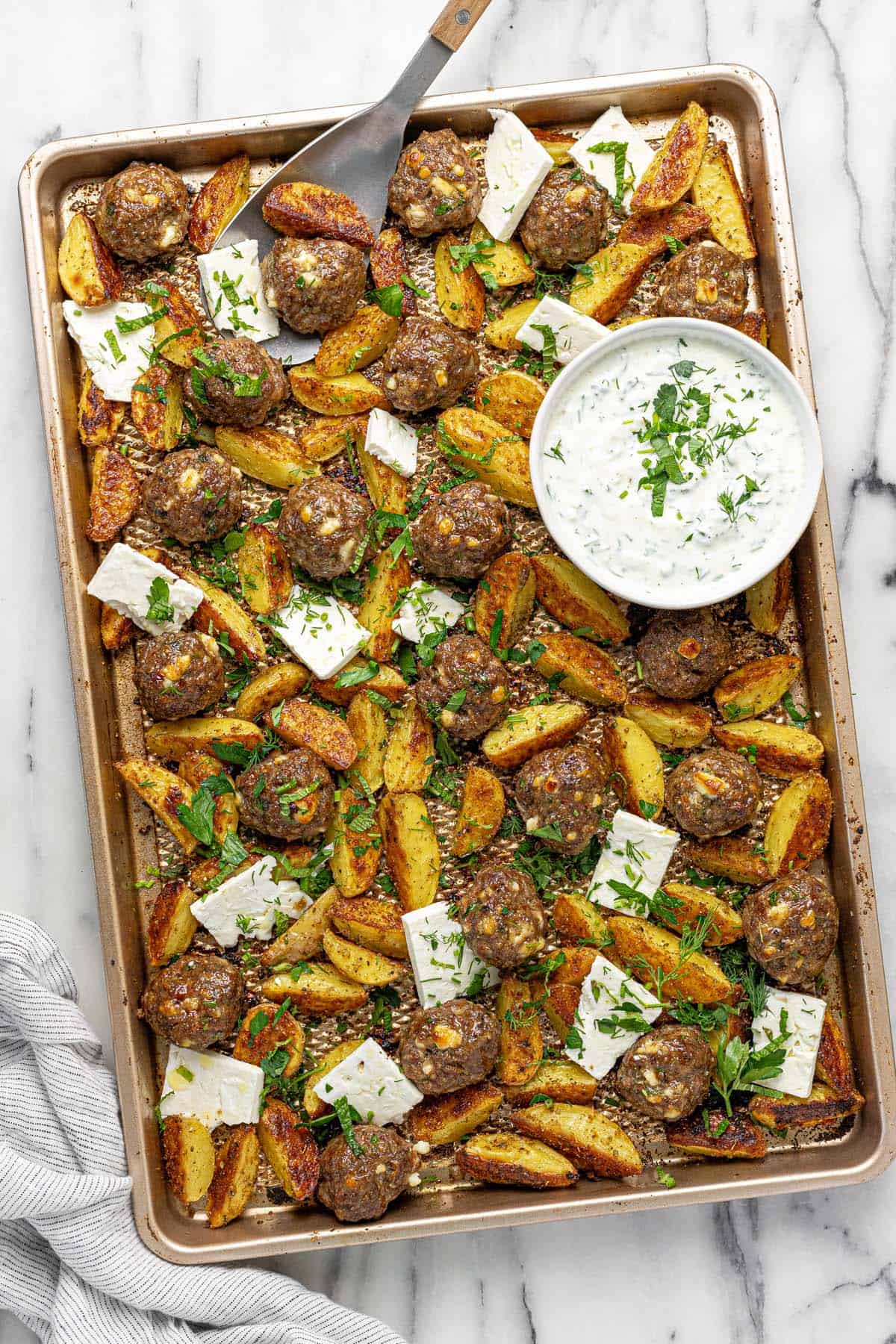 Sheet pan with meatballs, roasted potatoes, sliced feta, and fresh herbs.