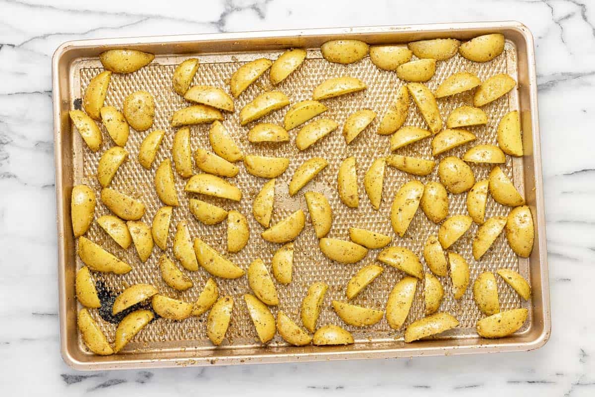 Sheet pan with quartered potatoes seasoned with herbs and olive oil.