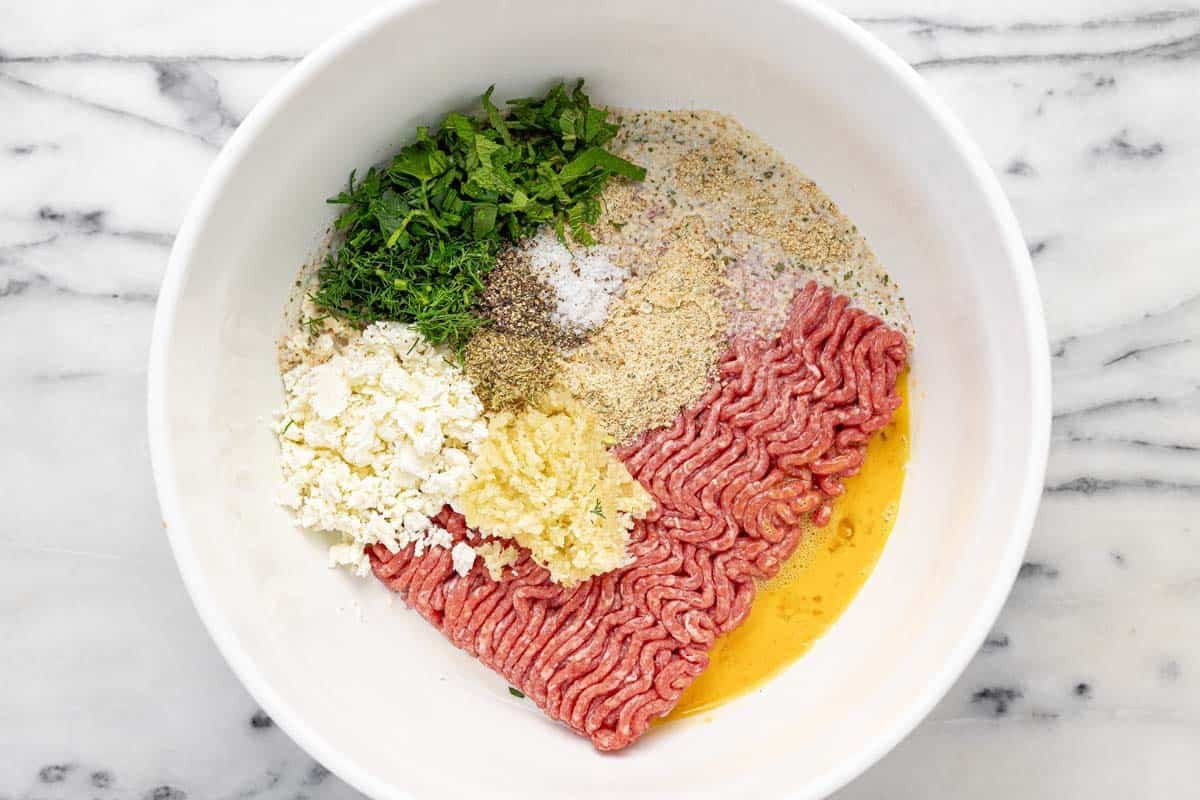 Large bowl filled with ingredients for Greek meatballs.