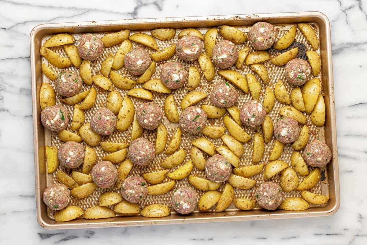 Raw meatballs and quartered potatoes on a large sheet pan.