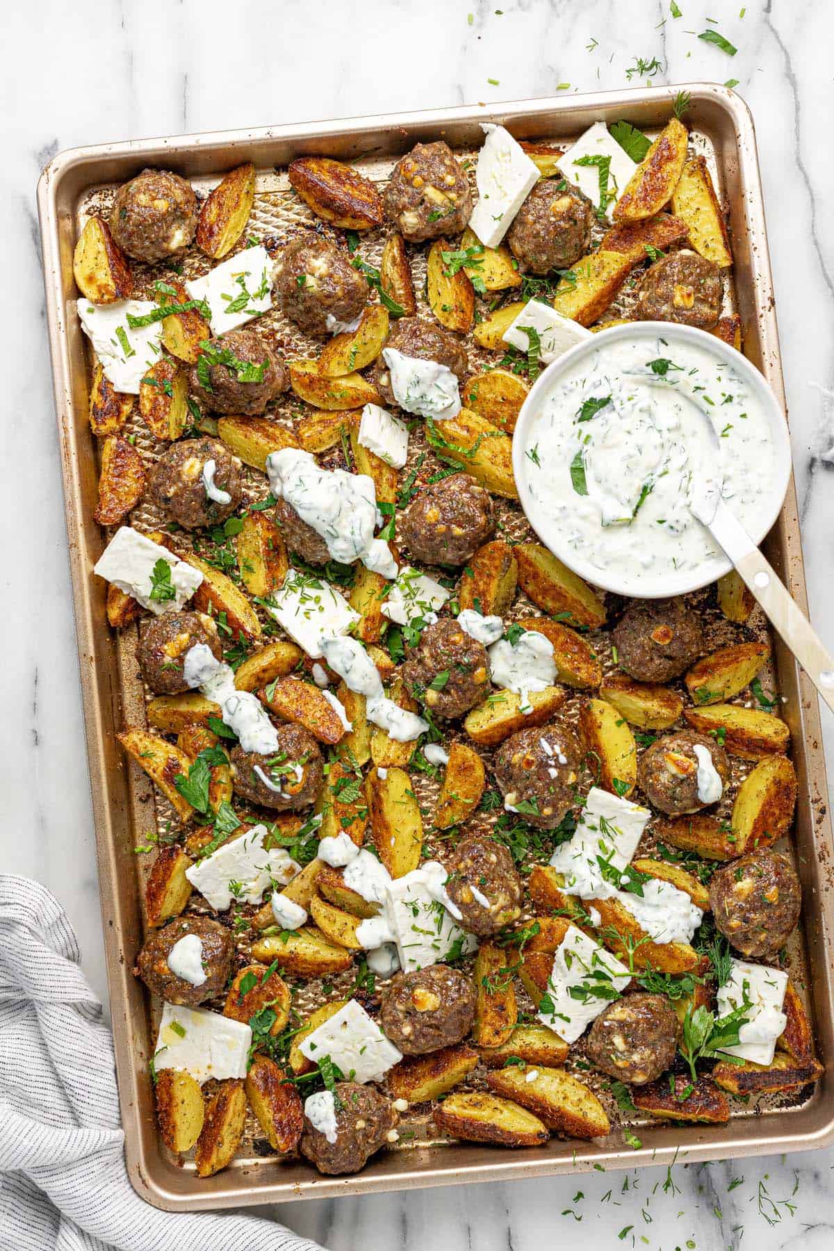 Sheet pan with meatballs, roasted potatoes, sliced feta, and fresh herbs.