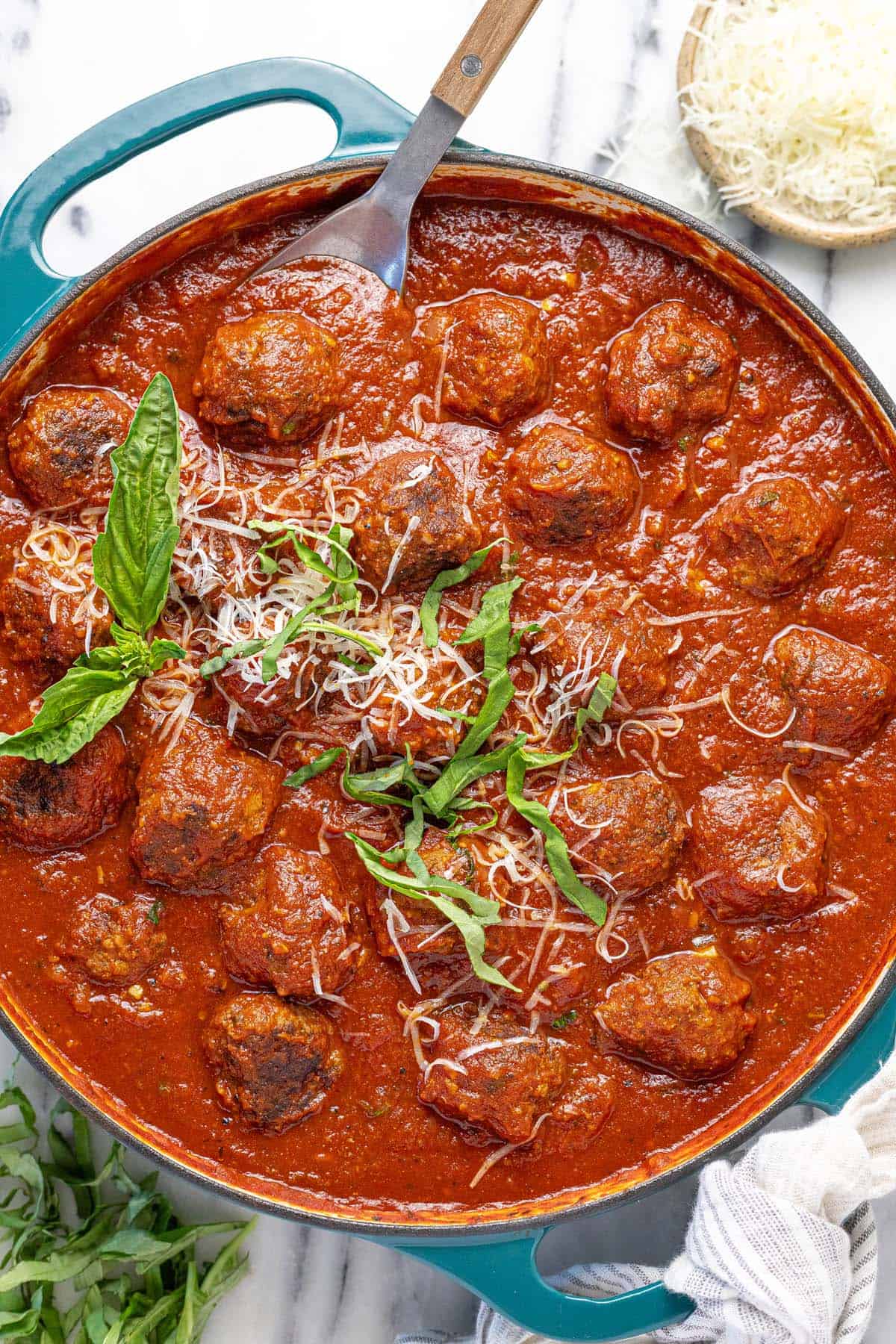 Large pan of meatballs in red sauce garnished with Parmesan and basil. 