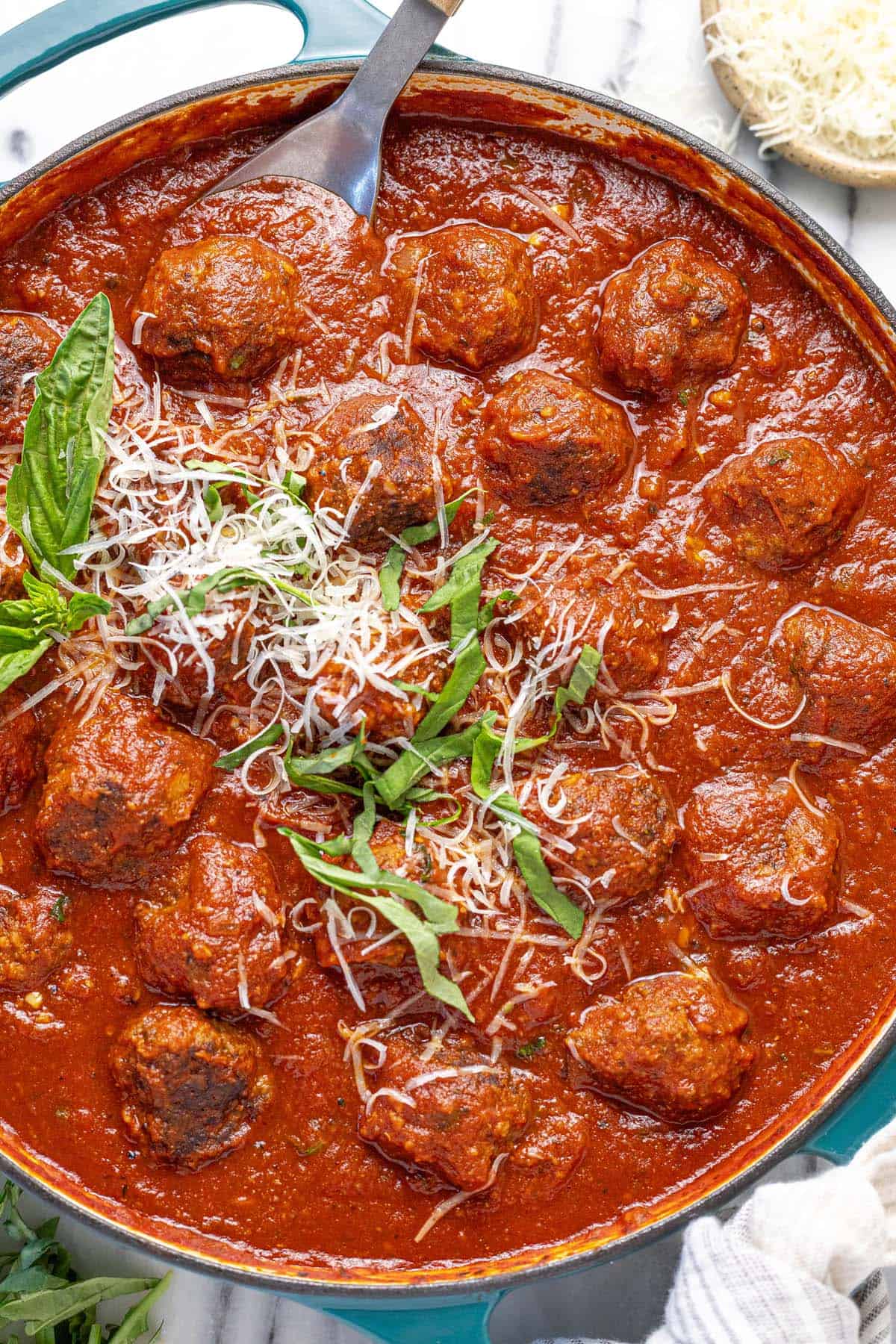 Large pan of meatballs in red sauce garnished with Parmesan and basil.
