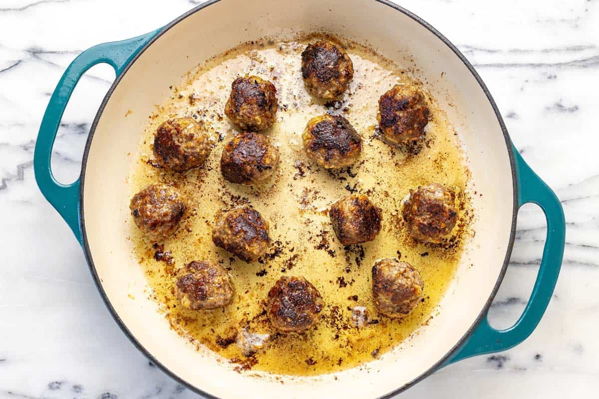 Pan with seared ground beef meatballs and oil.