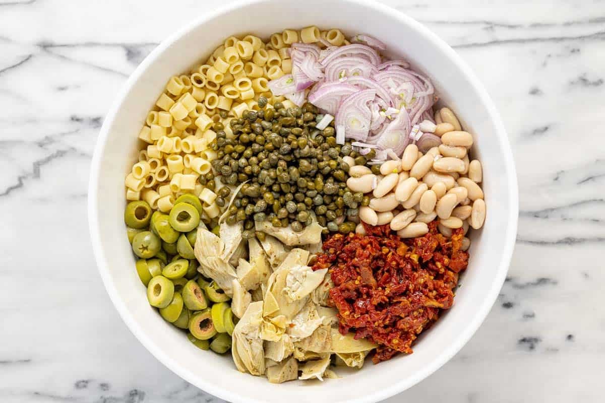 Large bowl filled with ingredients to make marinated white bean pasta salad.