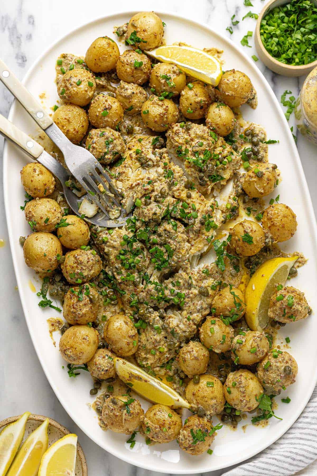 Serving platter filled with roasted potatoes and baked fish in mustard sauce. 
