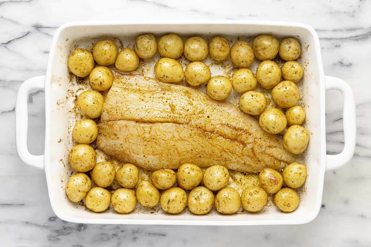 Baking dish filled with potatoes and fish tossed in herbs and spices. 