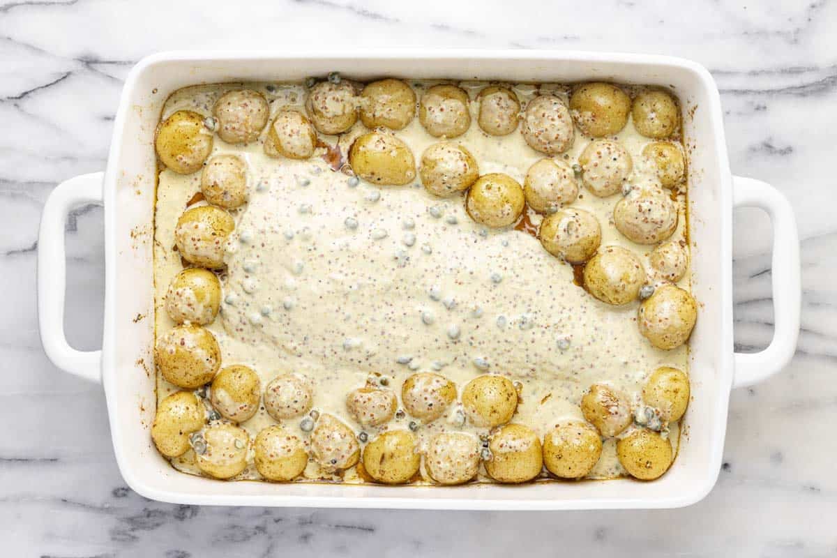 Mustard sauce poured over fish and potatoes in a large baking dish. 