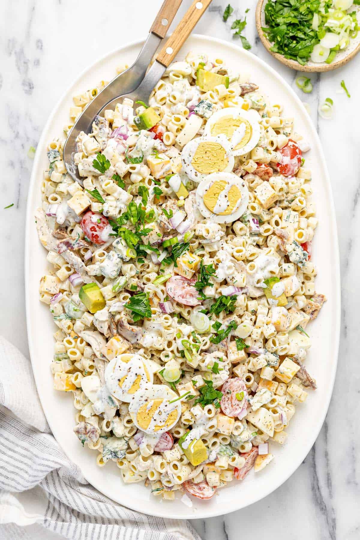 Large platter filled with cobb pasta salad garnished with fresh herbs.