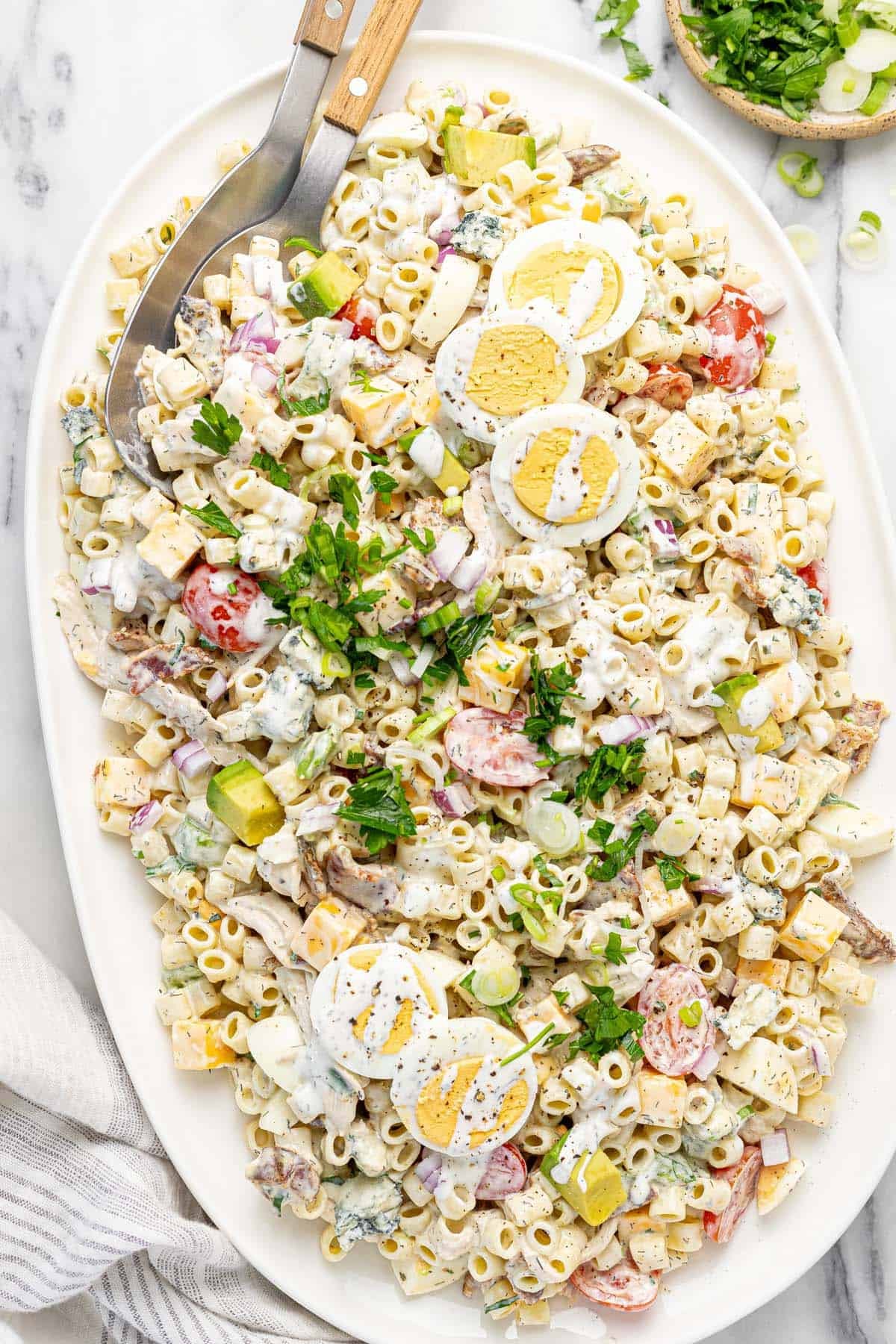 Large platter filled with cobb pasta salad garnished with fresh herbs. 