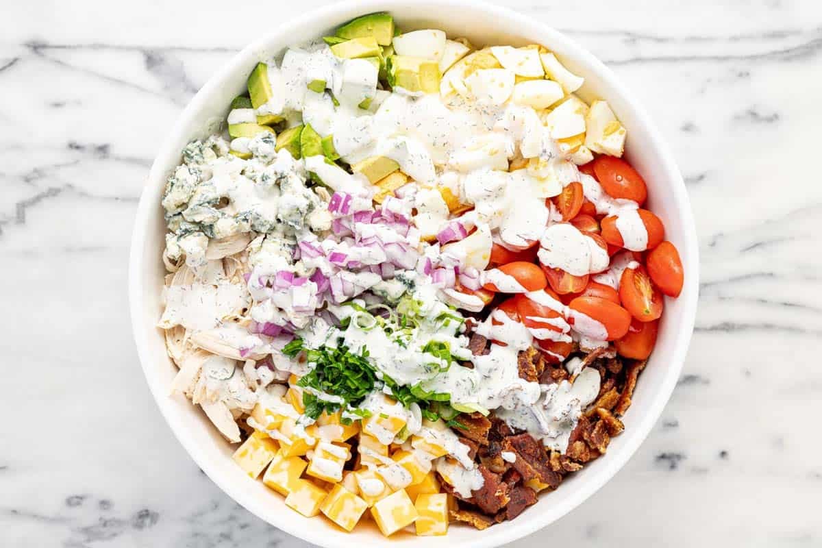 Dressing drizzled over cobb pasta salad in a large bowl.