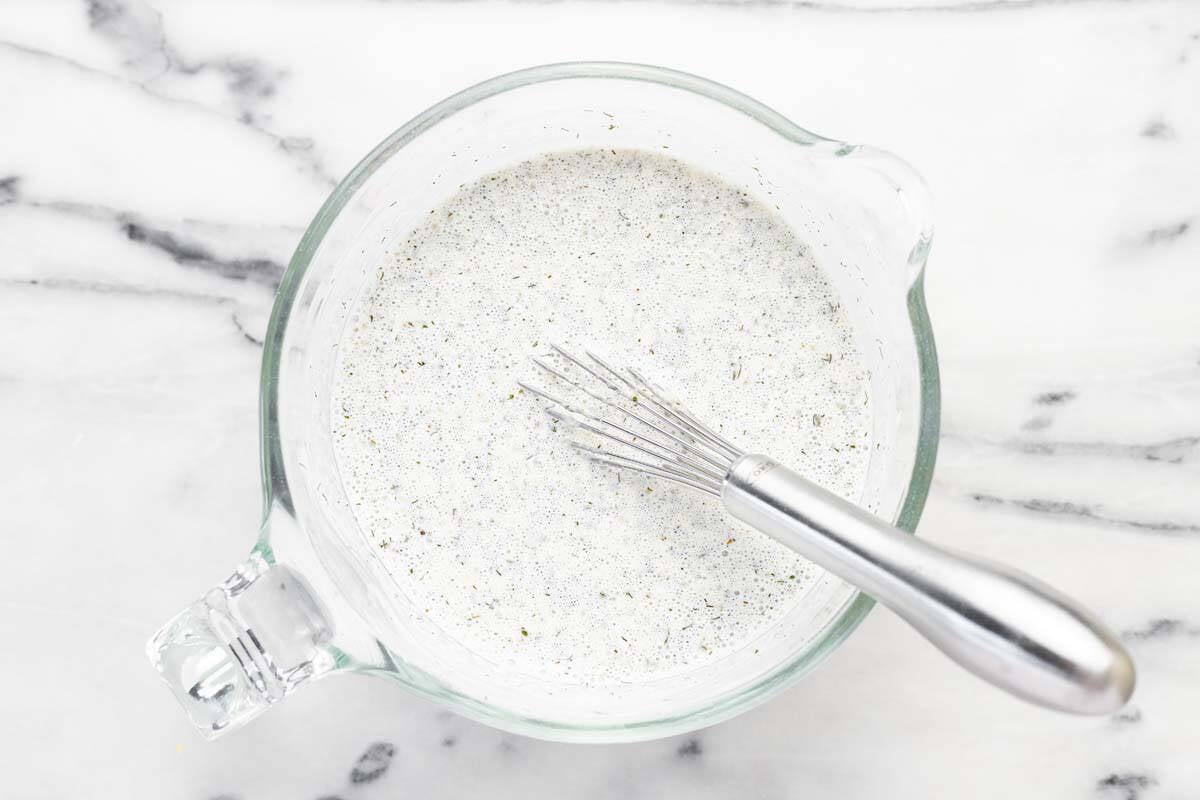 Large measuring cup filled with homemade ranch dressing and a whisk.