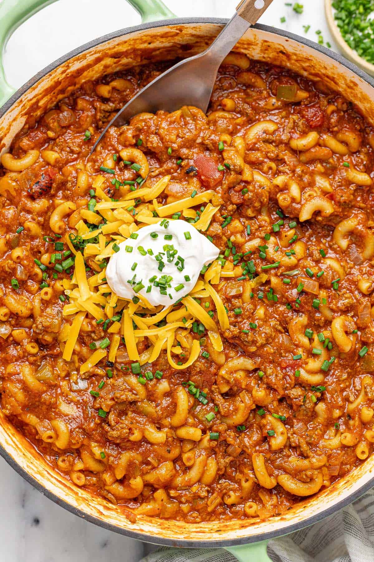 Large pan filled with cheesy American goulash topped with sour cream and shredded cheese.