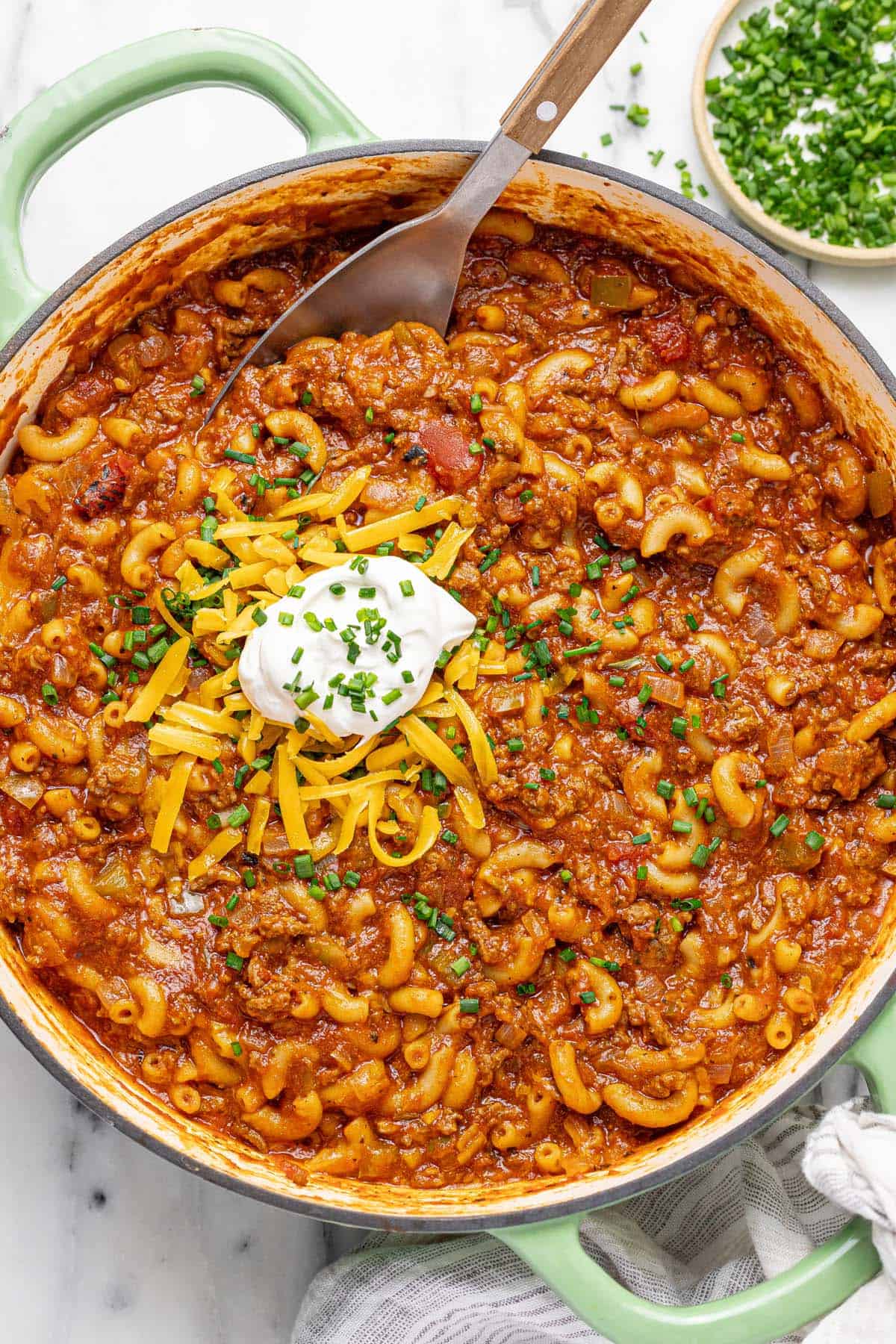 Large pan filled with cheesy American goulash topped with sour cream and shredded cheese. 