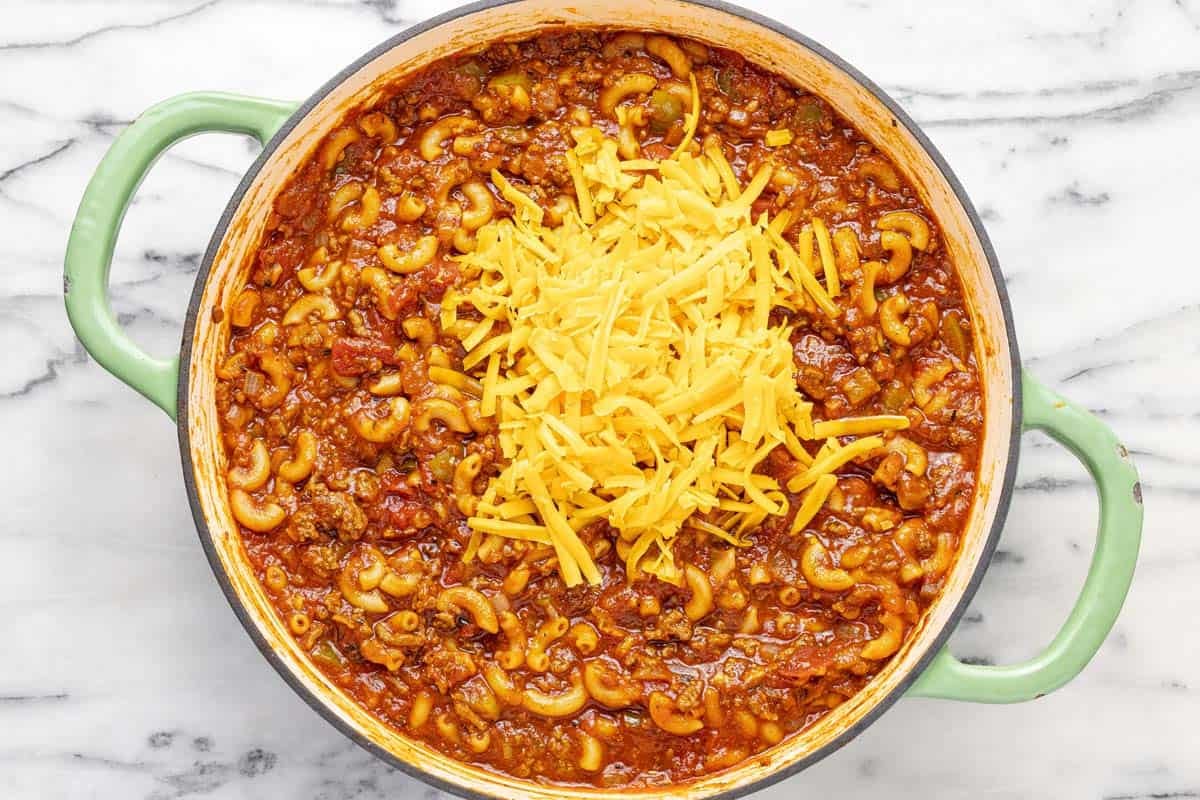 Shredded cheese added to a large pan of homemade goulash.