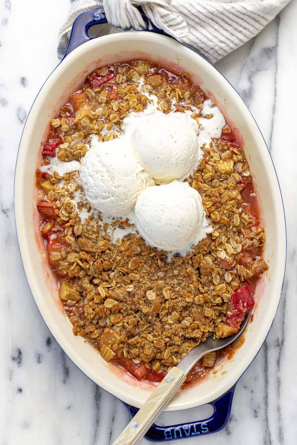 Baking dish with homemade rhubarb crisp topped with three scoops of ice cream. 