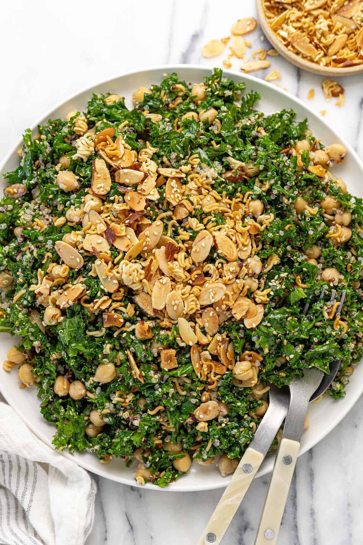 Large plate filled with sesame kale and quinoa salad topped with almonds, ramen, and sesame seeds.